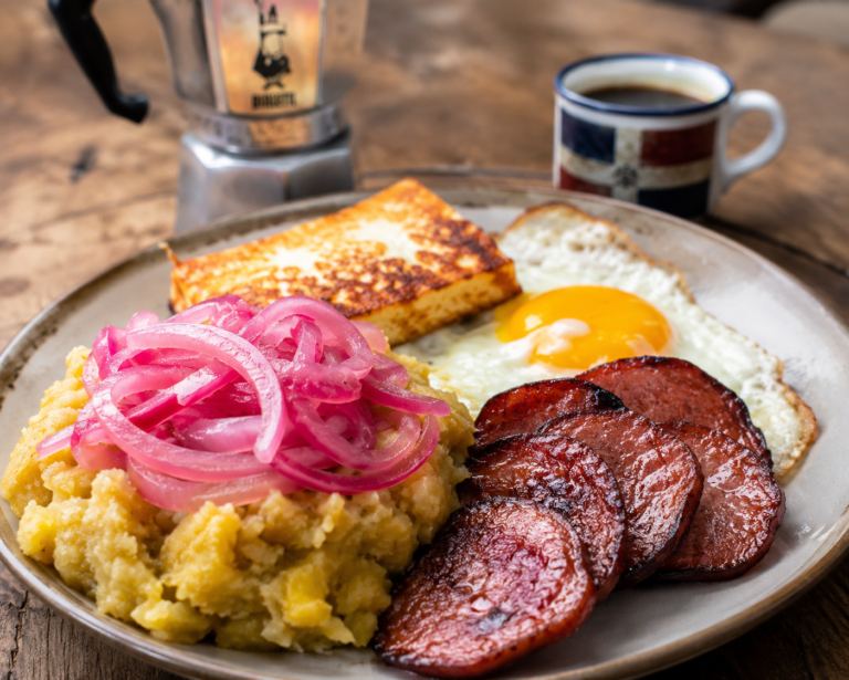 Plated tres golpes breakfast with mangu, fried cheese, salami, and a fried egg, served with Dominican coffee