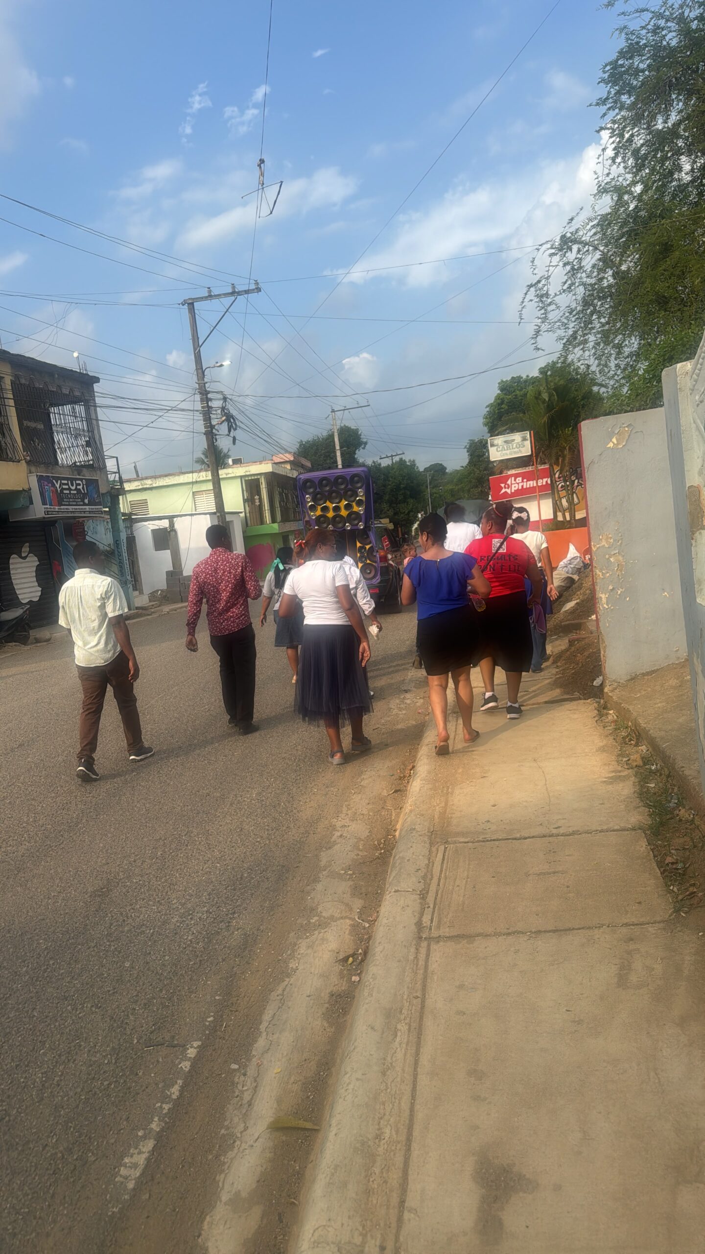 Street scene in Yamasá with an oversized car-audio speaker rig, people with their backs to the camera